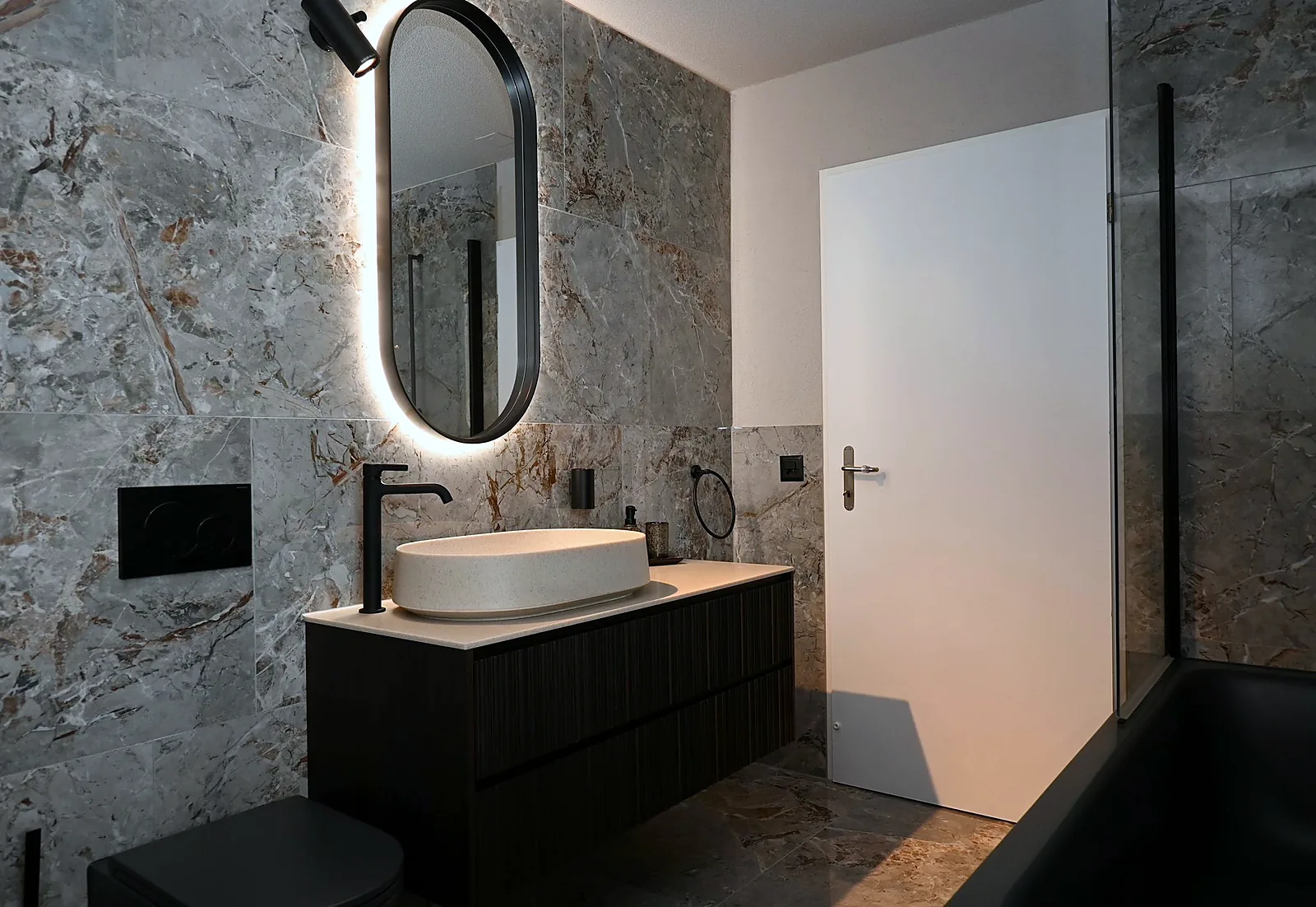 Badezimmer in grauer Marmoroptik mit schwarzen Armaturen und Badewanne